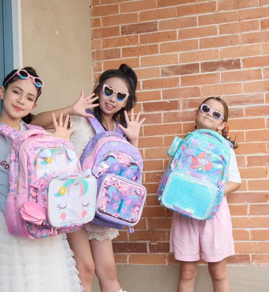 Three girls in heart sunglasses showing off unicorn, butterfly and mermaid backpacks with matching lunch bags
