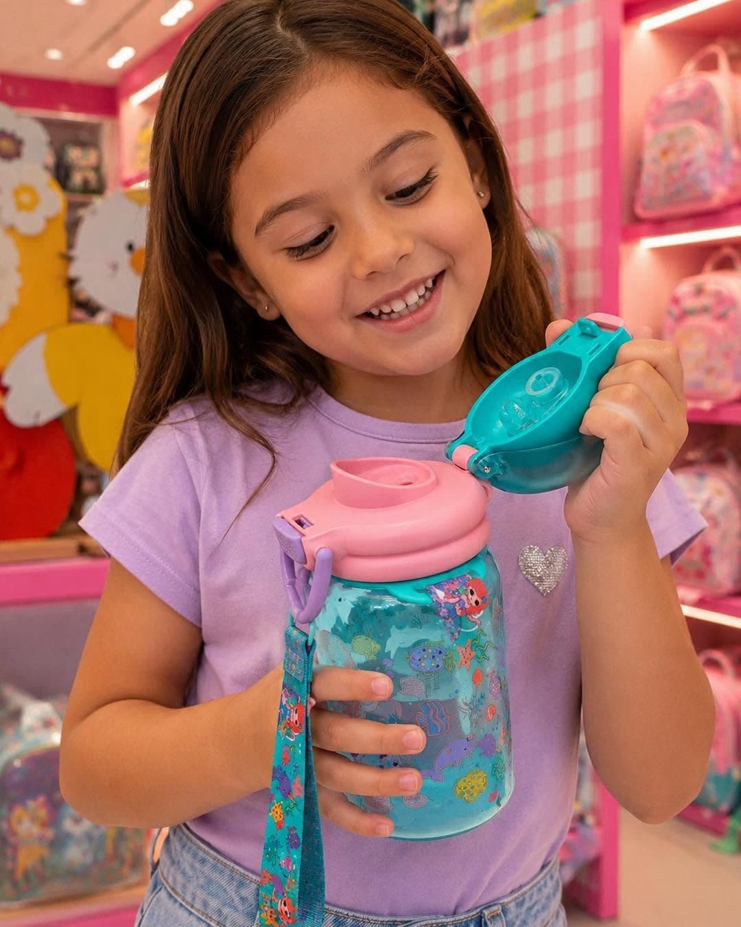 Smiling girl in the shop opening the lid of a turquoise mermaid water bottle